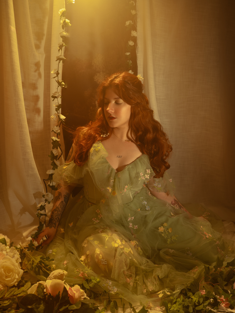 Woman in a floral dress sitting among flowers with a warm soft light.