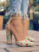 Beige high-heeled shoes with floral embroidery worn with ripped jeans on a blurred outdoor background.