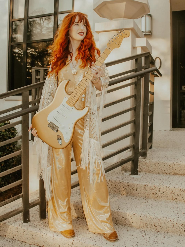 Woman with red hair holding a guitar outdoors on a staircase