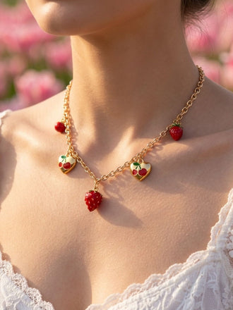 Necklace with red strawberry pendants worn by a person in a blurred pink floral background
