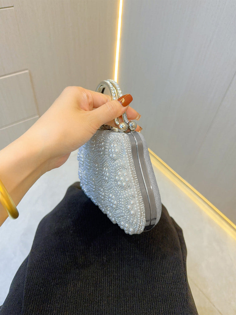 Hand holding a silver beaded clutch against a neutral background