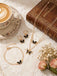 Jewelry set with butterfly details on a lace tablecloth with a book and cup of coffee.