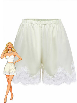 High-waisted cream satin pajama shorts with a delicate white floral lace hem, shown next to a retro pin-up style fashion illustration.