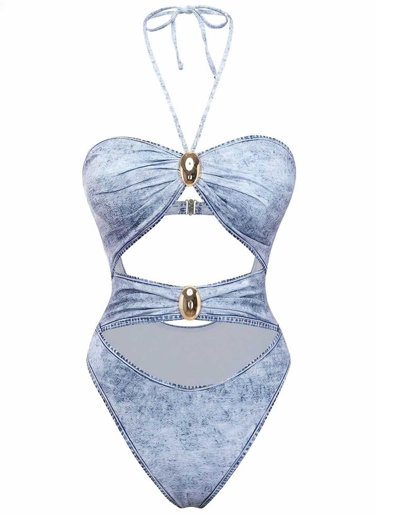 A light blue denim-print one-piece swimsuit featuring a halter neckline, multiple front cut-outs, and decorative gold-tone hardware accents.