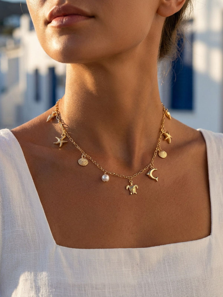Close-up of a woman wearing the gold sea-themed necklace with a white linen shirt against a coastal background.