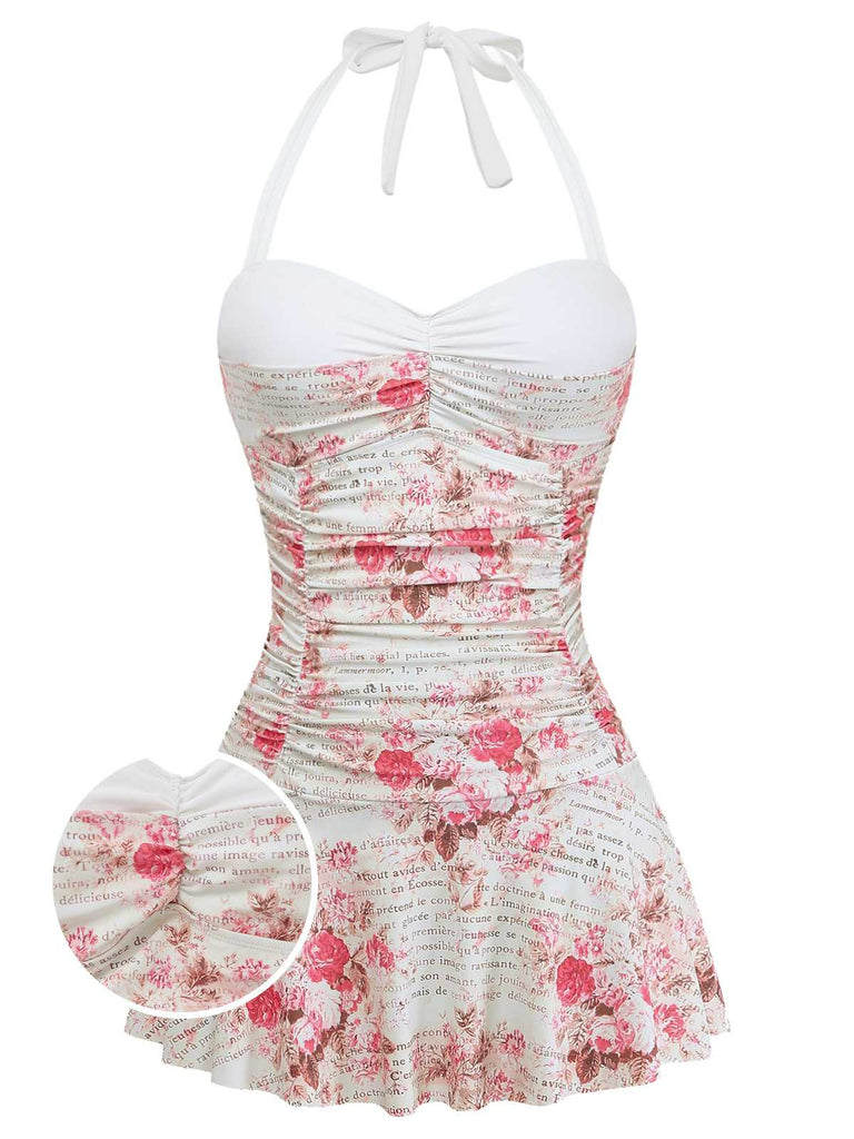 A white one-piece swimsuit featuring a pink rose print, vintage cursive script, a sweetheart neckline, and an attached ruffled swim skirt.