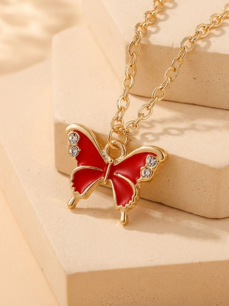 Red butterfly pendant necklace with gold chain on beige background