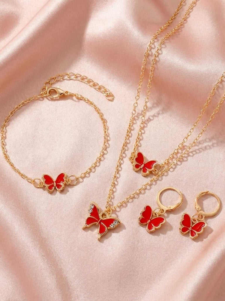 Gold jewelry set with red butterfly charms on a pink fabric background