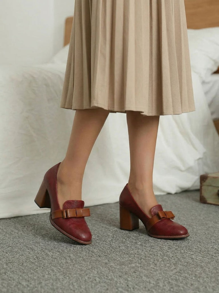 Red shoes with brown bow details worn by a person in a beige skirt.