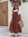 Front view of the pinafore-style maxi dress in rust brown featuring shoulder ties and a pleated skirt.