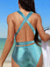 Rear view of the model wearing the teal swimsuit, highlighting the elegant criss-cross back strap design.