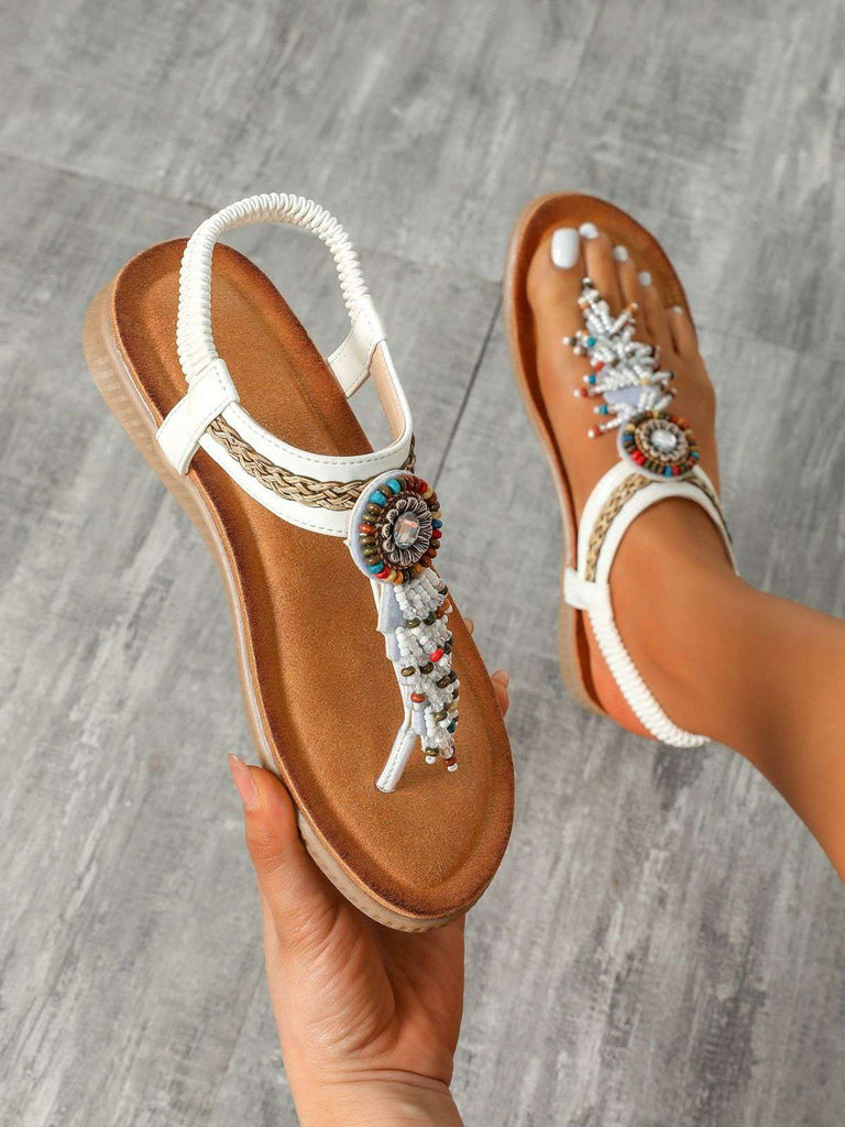Beaded sandals with tan soles on a gray wooden floor